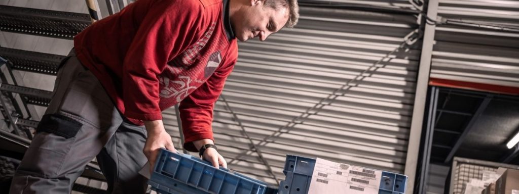 Mitarbeiter handhabt einen blauen Transportbehälter in einem industriellen Logistikbereich